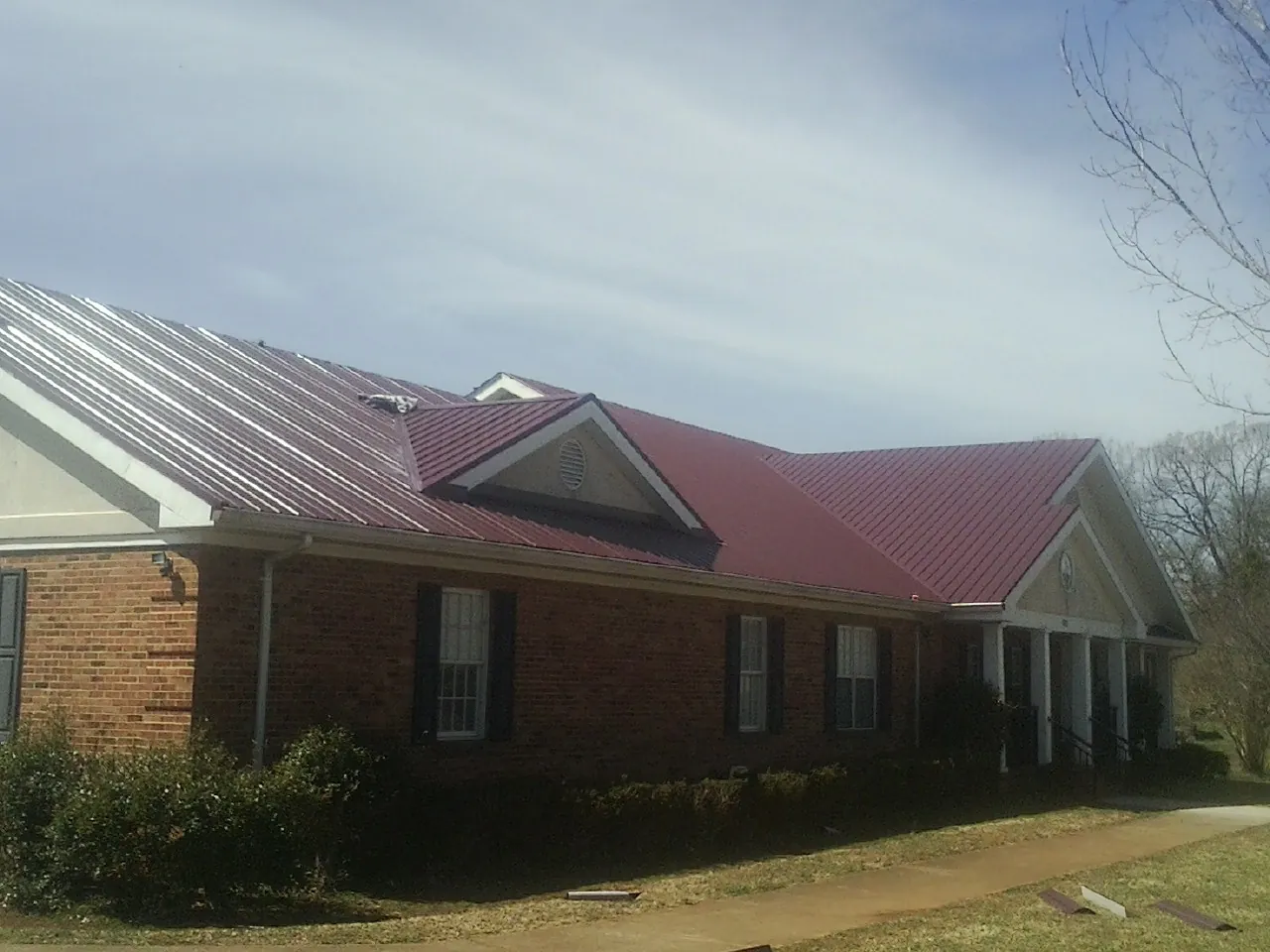 Red metal roof with gabled entries on a long brick building, from a Hail Damage Roof Repair job in Kewaskum