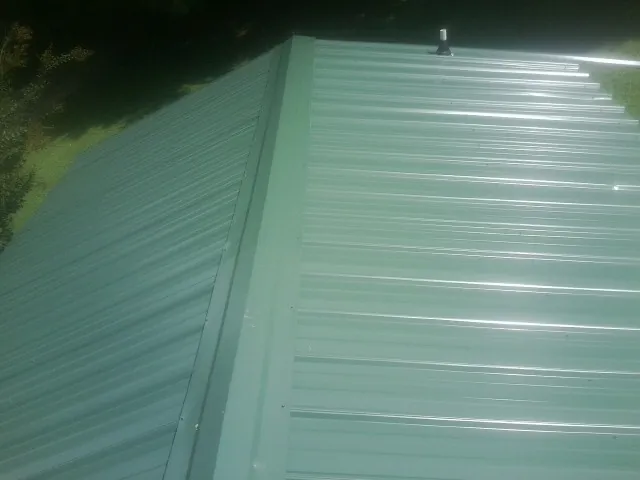 New green metal panels meeting at the ridge of a roof — Flat Roof Repair work by our crew in Kewaskum