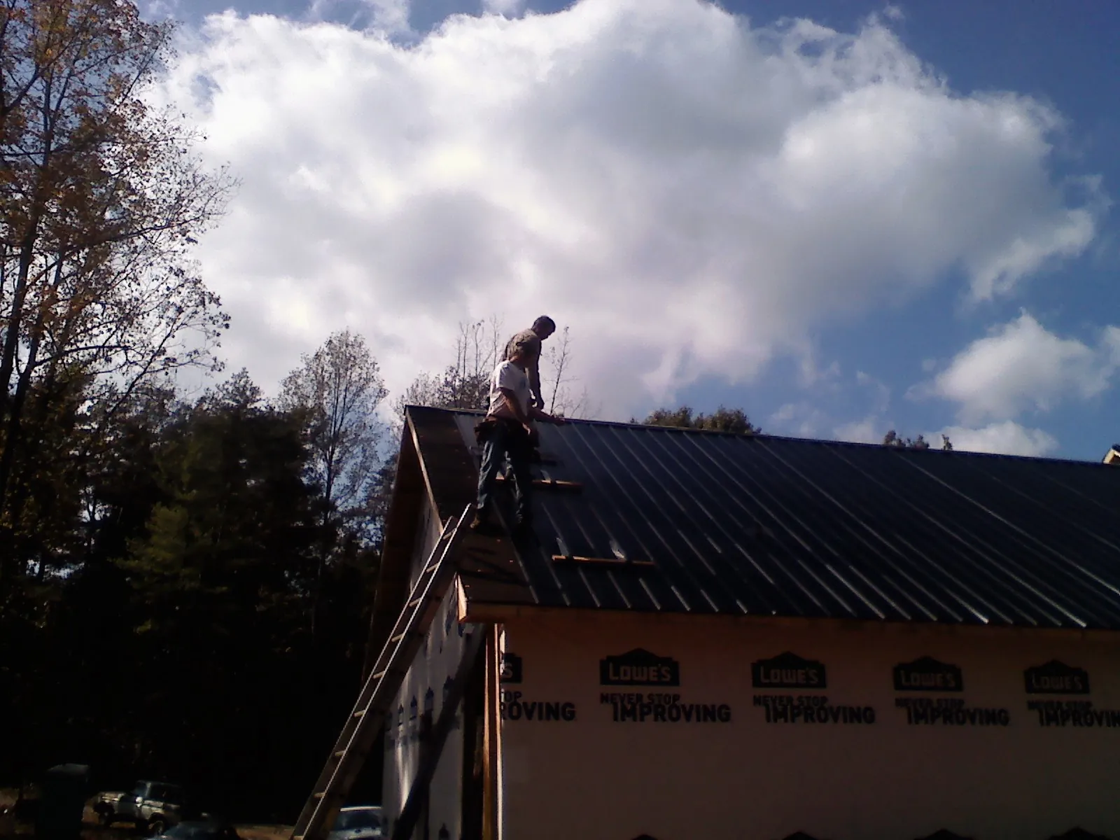 Roofer fastening dark metal panels high against a cloudy sky, from a Roof Inspection job in Kewaskum