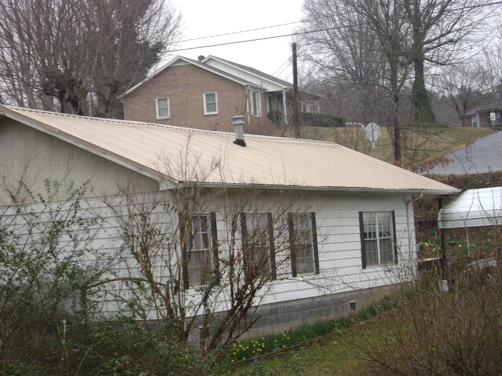 Tan metal roof on a white sided house set into a hillside — Commercial Roofing by Roofing Brothers in Kewaskum