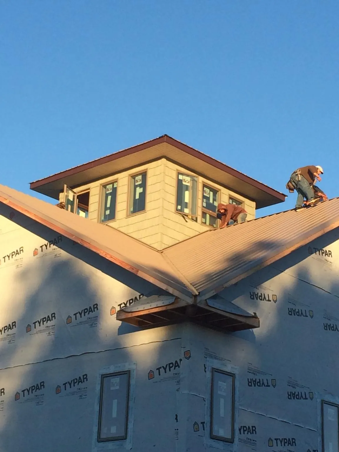 Roofers working around a rooftop cupola on a new metal roof at sunset — Roof Waterproofing in Kewaskum by Roofing Brothers